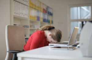 Frau schläft am Schreibtisch vor Laptop