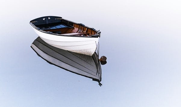 Einsames Boot spiegelt sich im ruhigen Wasser.