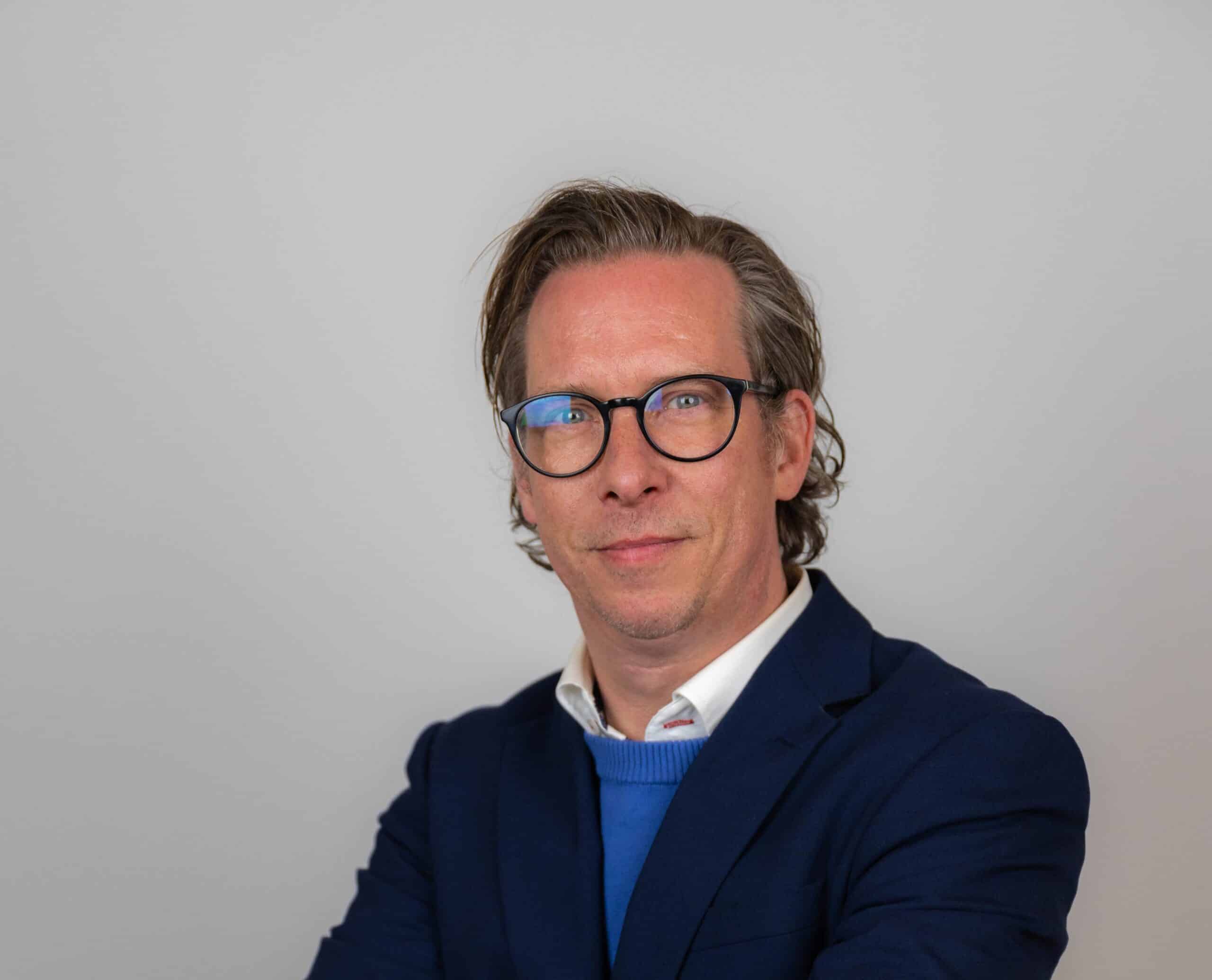 Person mit Brille im blauen Anzug lächelt leicht.